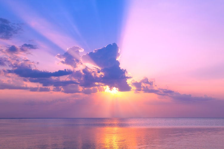 Sun behind pink clouds and above sea